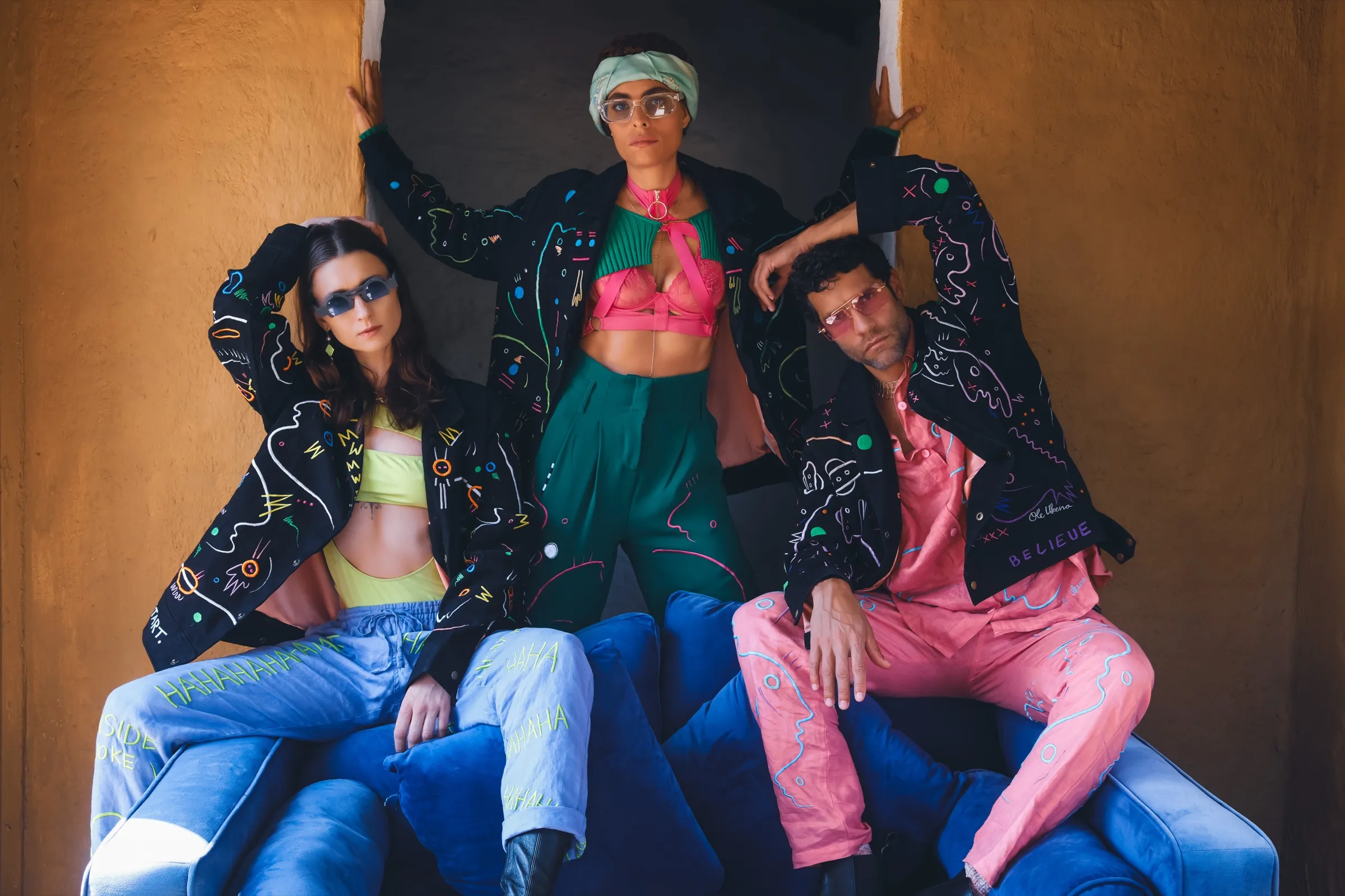 UKENA — three figures in hand-painted line-art jackets against a terracotta wall